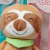 Une peluche de paresseux souriante avec un bandana vert à pois blancs.