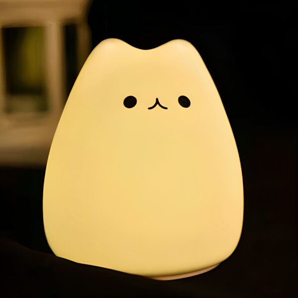 Une lampe en forme de chat en silicone jaune allumée, avec des yeux noirs et une bouche dessinée.